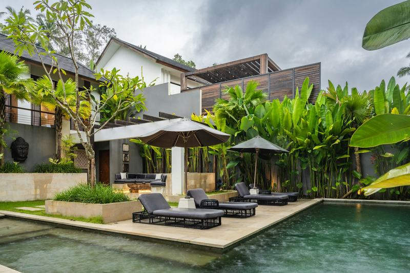 Villa pool with lounge chairs and tropical garden after rain in Bali