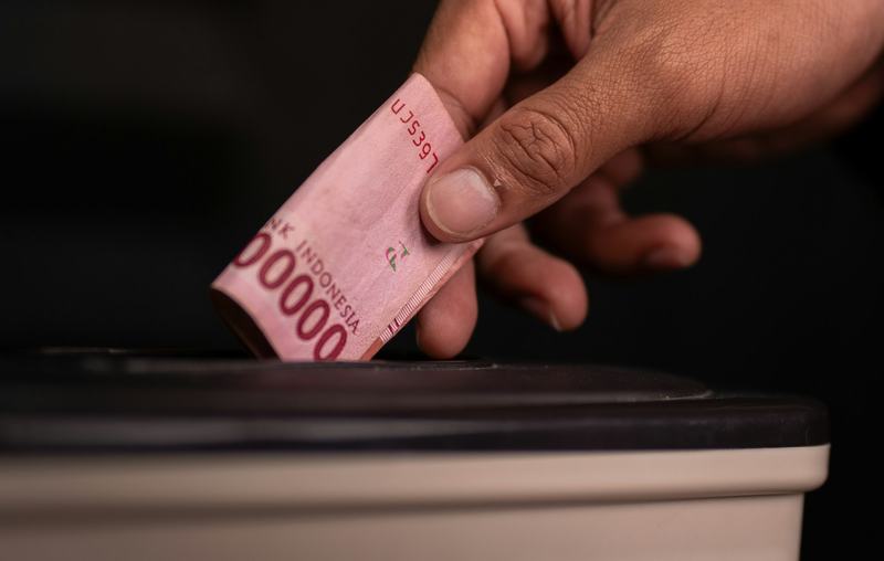 A hand feeding Indonesian banknotes into a machine