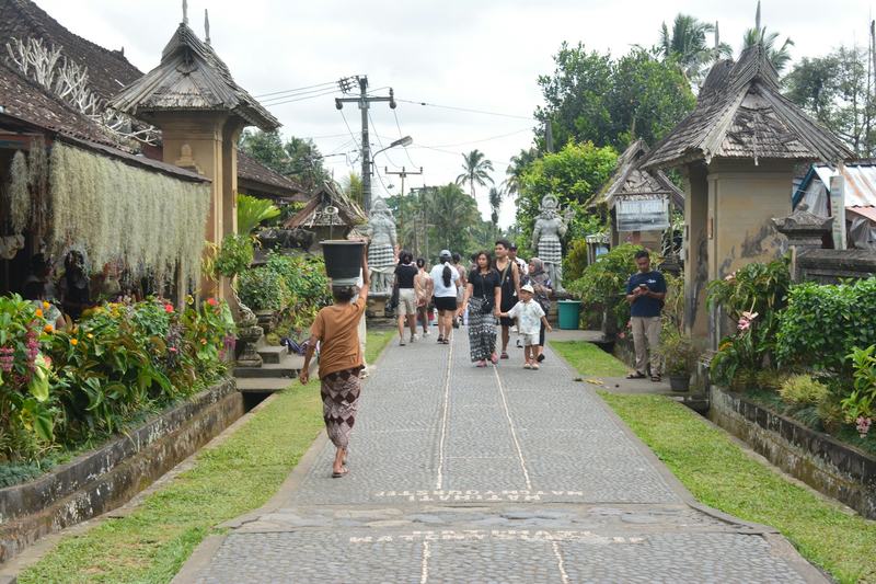 Rue d'un village balinais avec un portail traditionnel et des passants