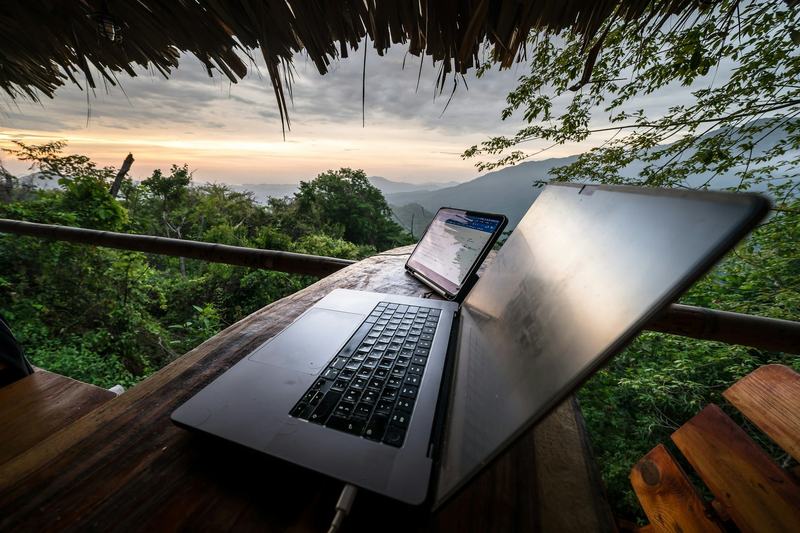A laptop and phone on a wooden terrace table with hills behind