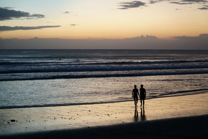 Two silhouettes walking along a Bali beach at sunset