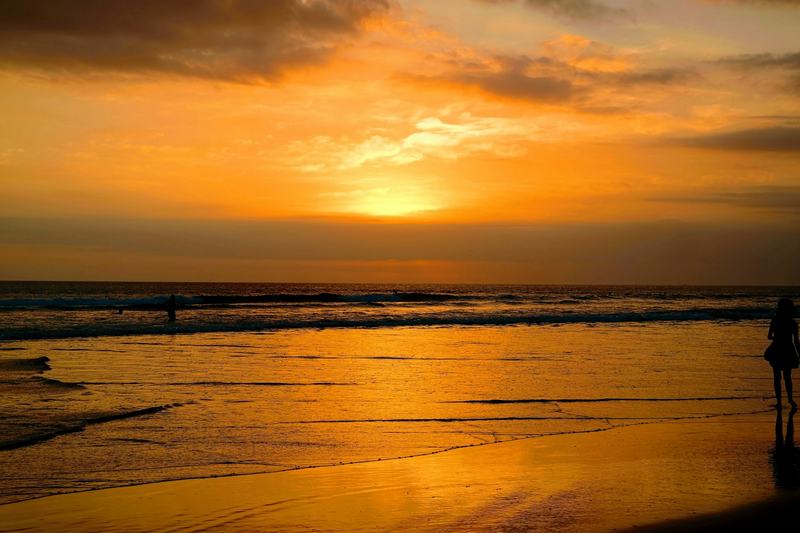 Sunset over a west-coast Bali beach, with surfers in the shallow waves