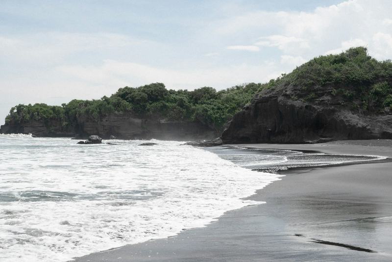 Black-sand beach in Pererenan with a green headland behind the surf
